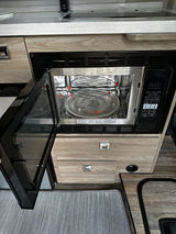 Inside an RV rental, an open microwave oven reveals its interior and control panel, part of the compact kitchen setup.