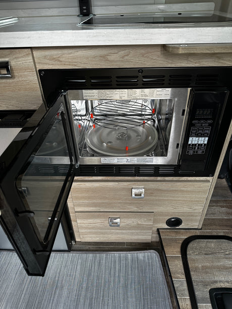 Inside an RV rental, an open microwave oven reveals its interior and control panel, part of the compact kitchen setup.