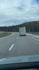 Rear view of an rv rental on a winding highway through a forest under a cloudy sky, ideal for a road trip.