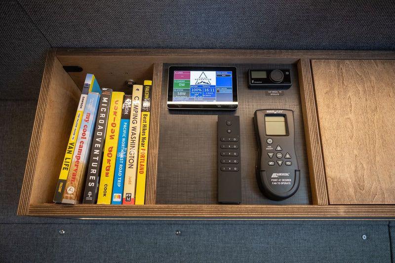 RV rental interior: shelf with travel books, a control panel for power/water, and remotes for climate & other systems. — photo 12