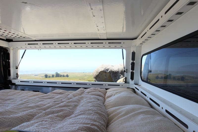 Cozy bed inside an RV rental offering scenic views of coastal hills & ocean. Ideal for camping adventures! — photo 5