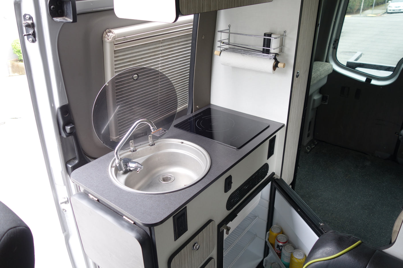 Compact rv rental kitchenette with sink, induction cooktop, fridge, and paper towel holder. Efficient use of space.