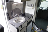 Compact rv rental kitchenette with sink, induction cooktop, fridge, and paper towel holder. Efficient use of space.