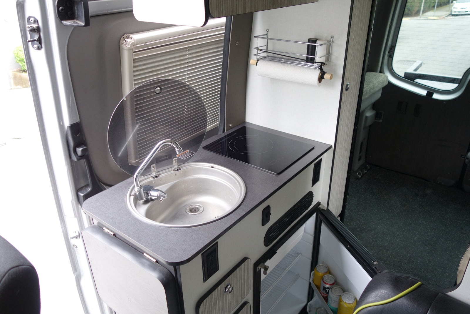 Compact rv rental kitchenette with sink, induction cooktop, fridge, and paper towel holder. Efficient use of space.