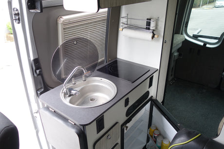 Compact rv rental kitchenette with sink, induction cooktop, fridge, and paper towel holder. Efficient use of space.