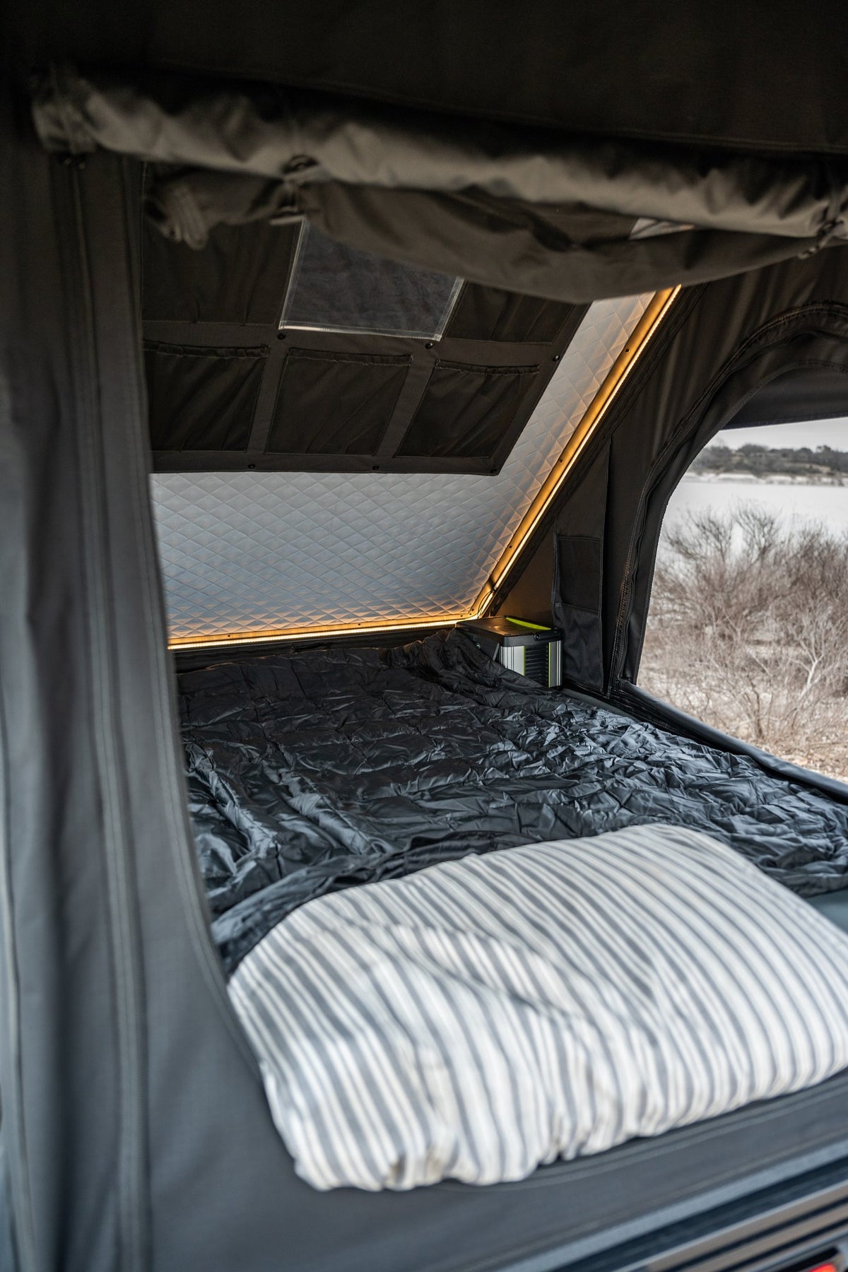 Inside the rooftop tent looking out the open door, showing the upgraded mattress with bedding, the quilted insulated ceiling panel, and the warm interior LED light strip running along the roofline — photo 4