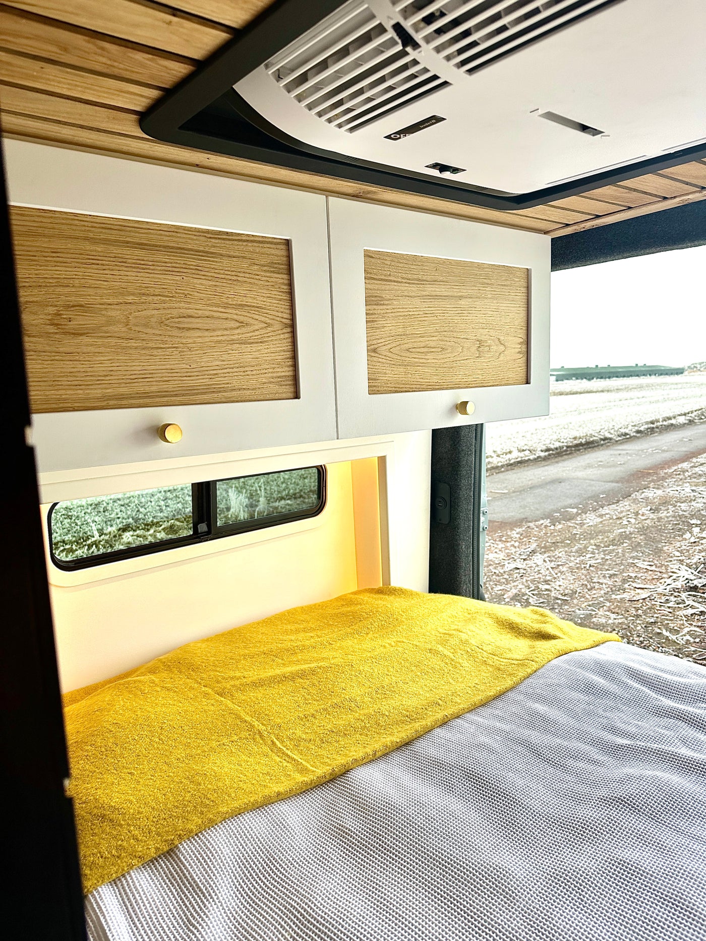 Cozy RV rental interior featuring a bed with yellow throw, modern white cabinets, and overhead AC unit. Ideal for travel. — photo 8