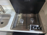 An RV rental's compact kitchen with a stainless steel sink, faucet, and a Dometic two-burner gas stovetop.