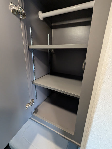 RV rental: View inside a small, grey cabinet with a white hanging rod, two adjustable shelves, and visible door hinges.