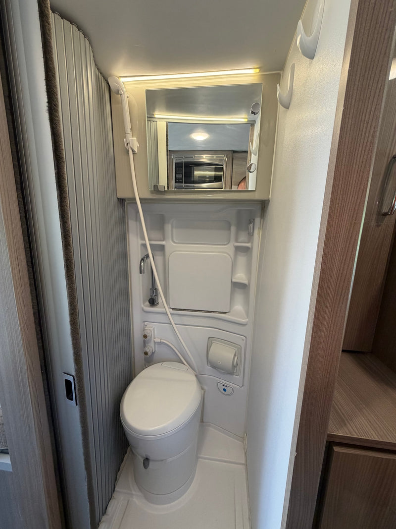 This RV rental bathroom maximizes space with a toilet, shower, and mirror, featuring a ribbed, retractable door. — photo 8