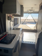 rv rental: Interior of a camper van featuring a compact kitchenette, sleeping area, and a bright sandy beach view out the rear window.