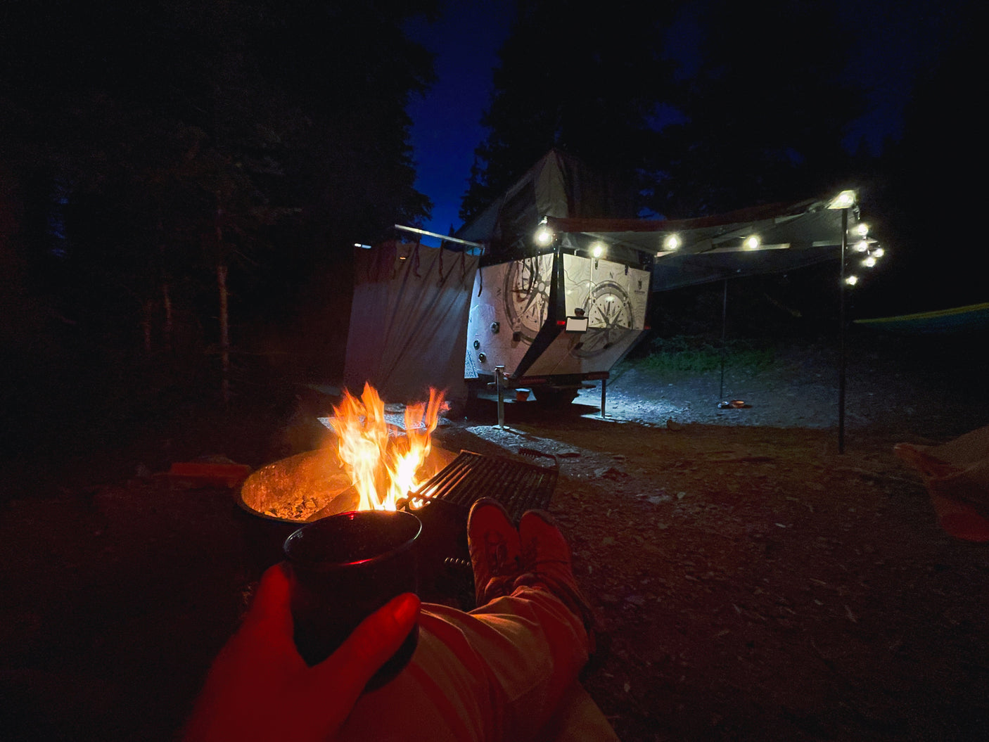 Warm campfire glow illuminating a night campsite scene with an eye-catching RV rental and decorative string lights.