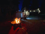 Warm campfire glow illuminating a night campsite scene with an eye-catching RV rental and decorative string lights.