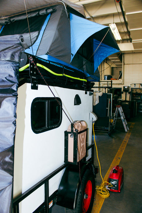 This RV rental trailer features a rooftop tent, ROAD SHOWER, and generator, ready for off-grid camping adventures.