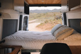 Cozy rv rental interior with a bed, patterned pillows, & a scenic view of a dirt road and mountains out the back.