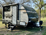 A sleek Forest River Aurora travel trailer, ideal for your next rv rental, parked on grass amidst mature trees.