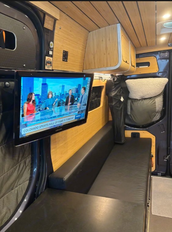 Camper van rv rental interior: bamboo walls, a TV showing news, and a black bench seat. Ideal for mobile living. — photo 9