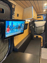 Camper van rv rental interior: bamboo walls, a TV showing news, and a black bench seat. Ideal for mobile living.