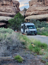 White RV rental at campsite 10, nestled between towering rock formations and green shrubbery. Great for outdoor adventures.