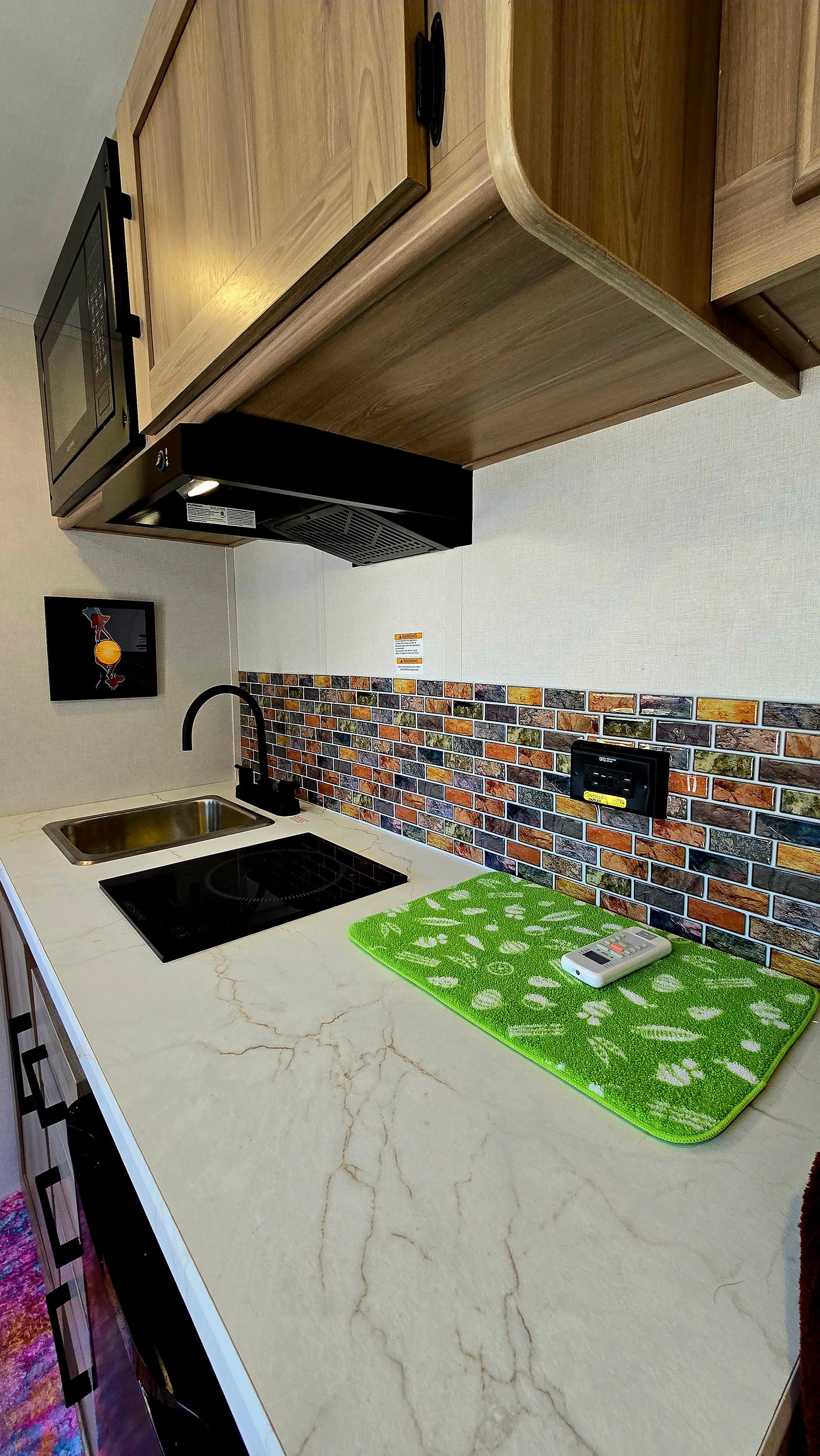 Sleek RV rental kitchen with induction cooktop, sink, microwave, bright marble-look counter & colorful brick backsplash.