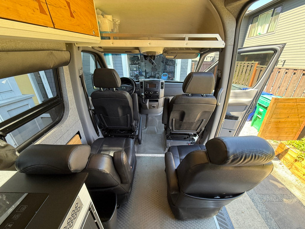 This RV rental interior features swiveling front seats facing the living area, with an open side door to outside.