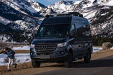 Dark gray Sprinter RV rental parked in snowy mountains with a child playing.