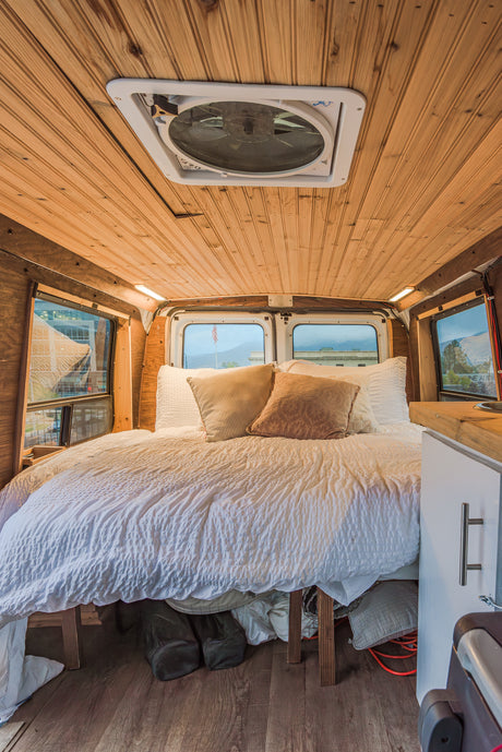 Cozy RV rental interior featuring a comfortable bed, wooden paneling, roof fan, and window views.