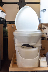 Inside an rv rental, a white composting toilet with an open lid, ready for sustainable travel and van life.