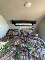Cozy RV rental bedroom with camouflage bedding, overhead light, and window. Ideal sleeping space for your adventure.