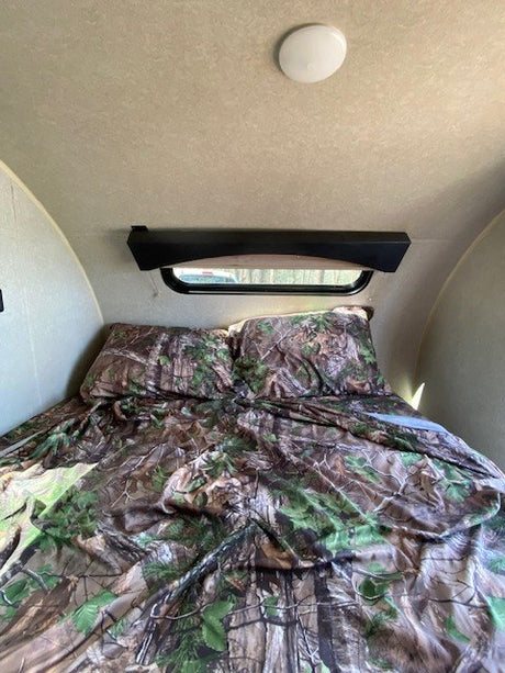 Cozy RV rental bedroom with camouflage bedding, overhead light, and window. Ideal sleeping space for your adventure.
