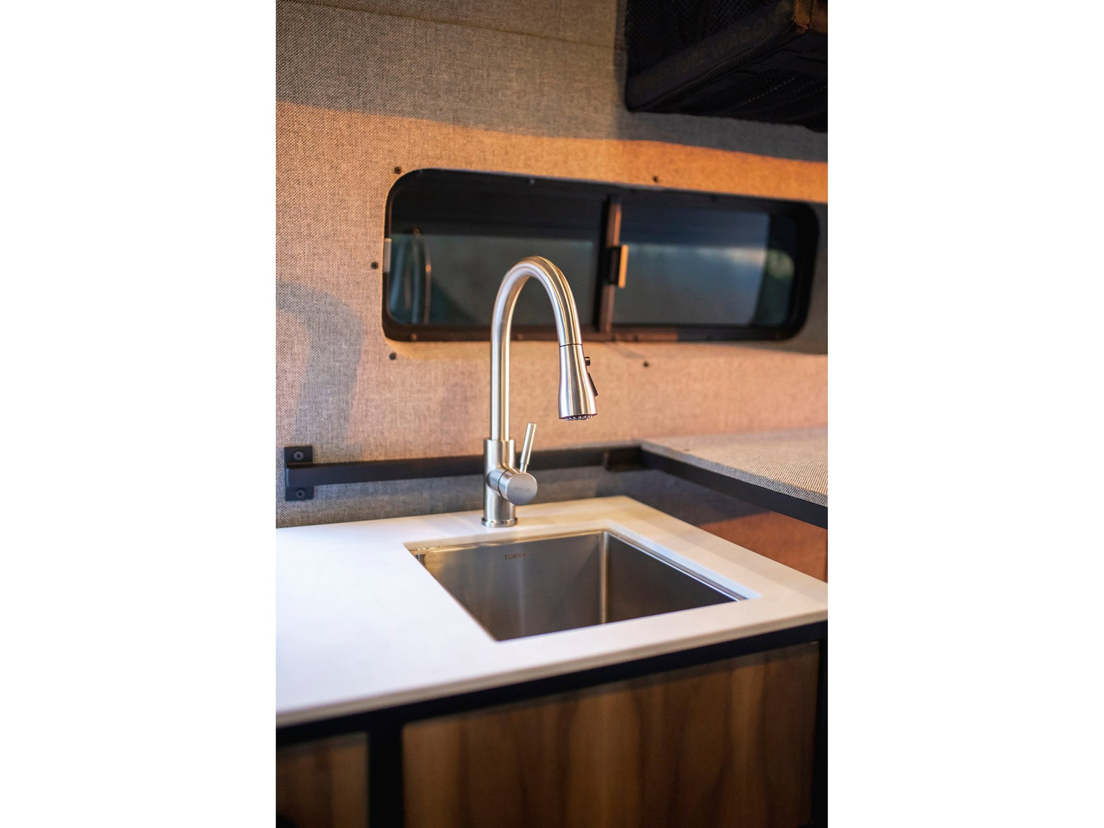 Enjoy a functional RV rental kitchen: sleek stainless steel sink, modern faucet, white countertop, and fabric walls.