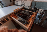 RV rental kitchen: a pull-out drawer reveals an induction cooktop. Cozy bed above, bike storage below.