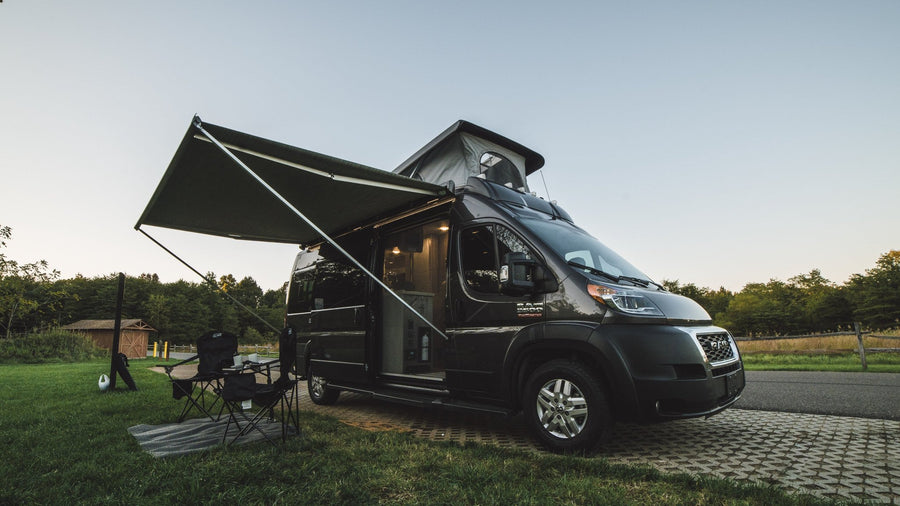 This RV rental camper van is set up for a relaxing campsite adventure, with an awning extended & pop-top raised.