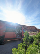 Red camper van parked with open door by red rocky cliffs on a sunny day. Your adventure starts with an RV rental!