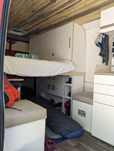 Inside an RV rental: a compact living space with raised bed, wooden ceiling, storage cabinets, and seating.