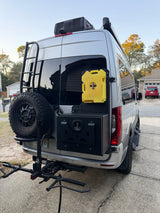 Silver Sprinter RV rental with rear-mounted spare tire, ladder, diesel canister, storage box, and bike rack.