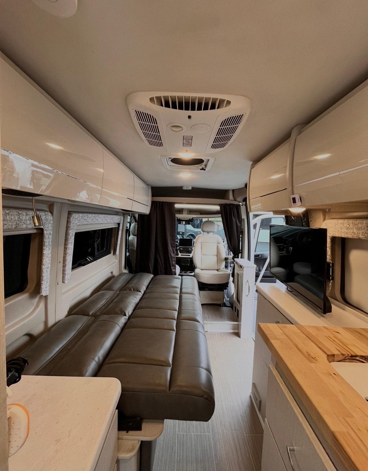 Inside a comfortable rv rental: showing a lounge bed, kitchen counter with sink, wall-mounted TV, and front cabin view.
