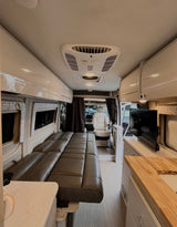 Inside a comfortable rv rental: showing a lounge bed, kitchen counter with sink, wall-mounted TV, and front cabin view.