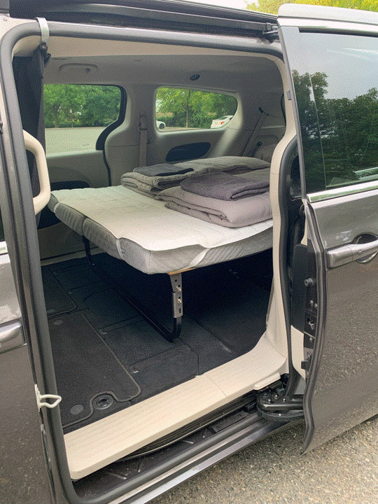 Inside an RV rental alternative: a minivan transformed into a cozy sleeping space with an elevated bed and bedding.