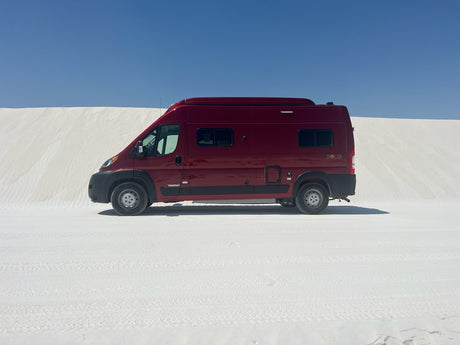 Red Winnebago Solis RV rental parked on white gypsum dunes under a clear blue sky, ready for desert adventure.