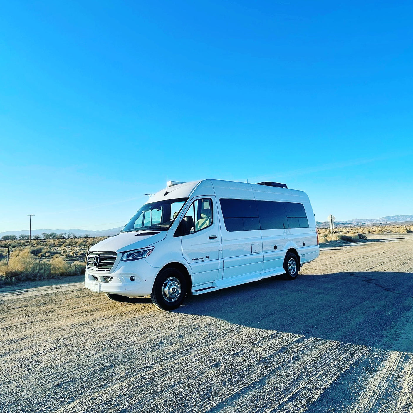 Ready for your next journey? This sleek white RV rental van is parked on a dusty road in a sunny desert landscape.