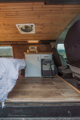Cozy camper van interior, perfect for an rv rental adventure. Features a bed, compact kitchen, and warm wooden finishes.