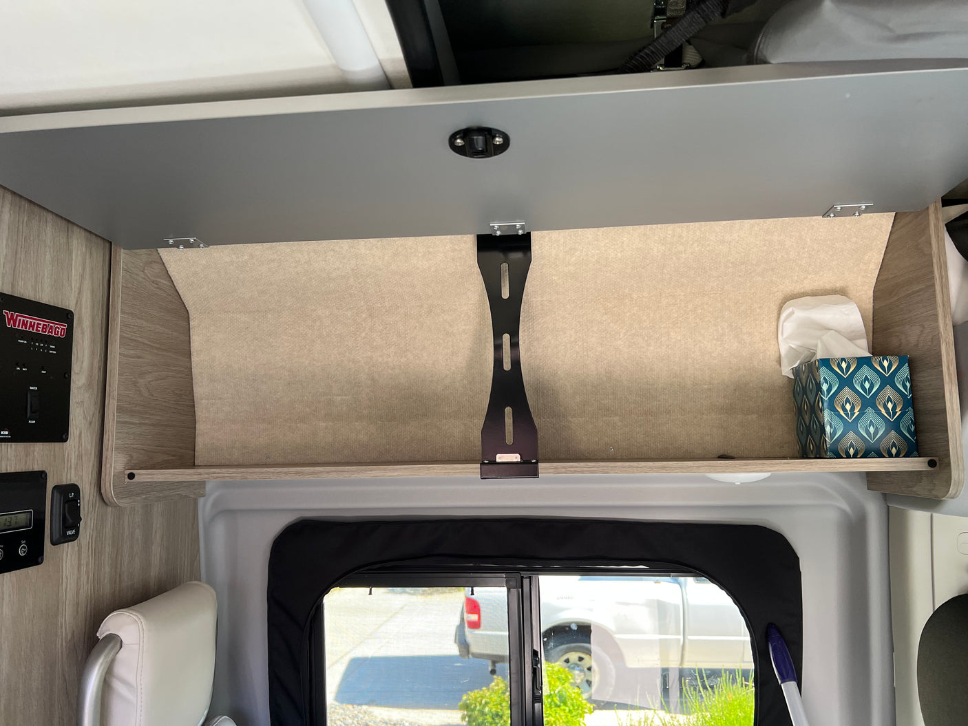 RV rental overhead cabinet showing tissue box, Winnebago control panel, & open storage space above a window.