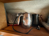Compact kitchen essentials on an RV rental shelf: silver pot & black electric kettle. Power cord visible for small space living.