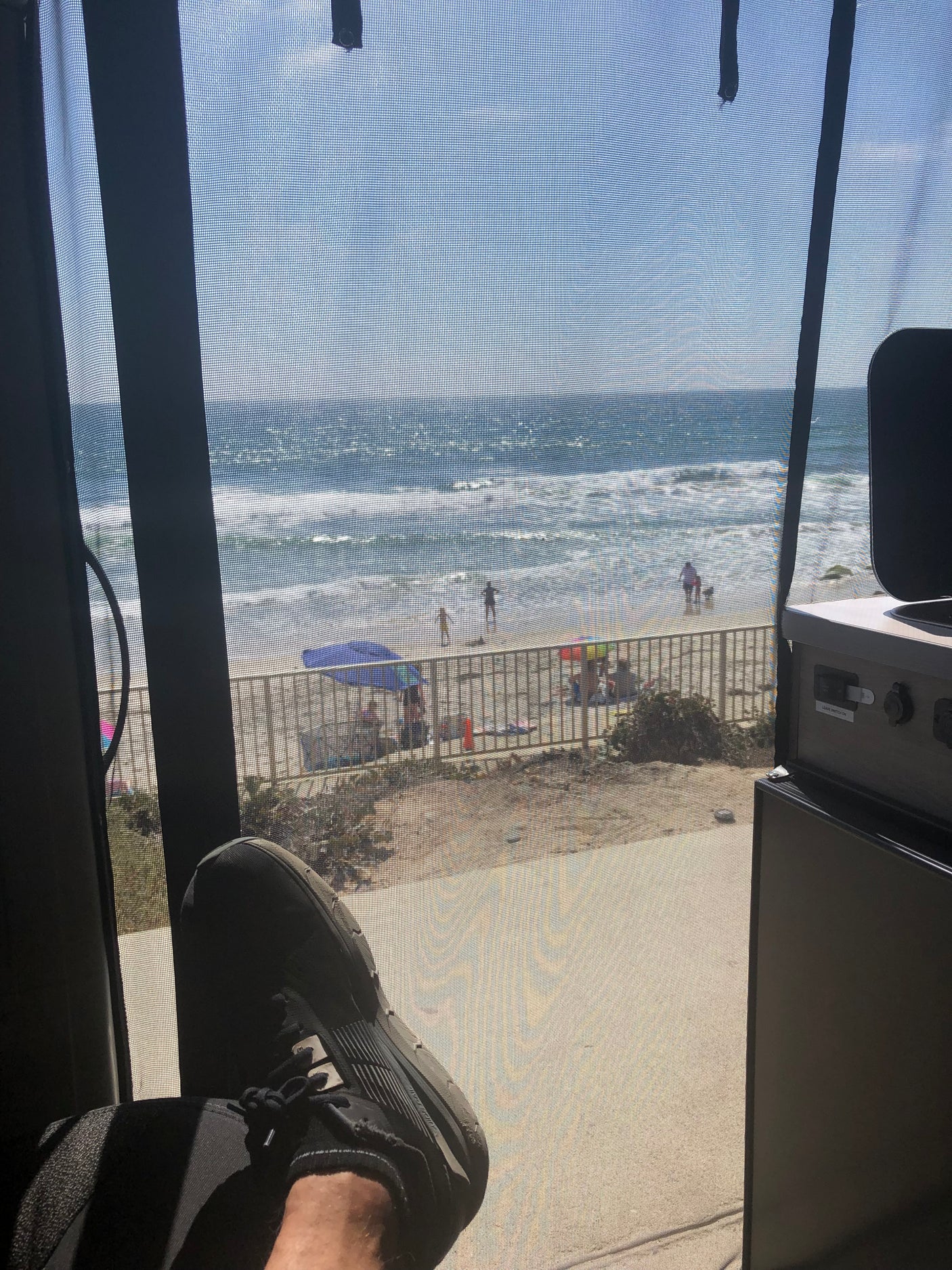 Relaxing in an RV rental with a stunning beach view through the screen, showing ocean waves, sand, and people.