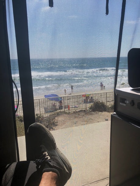Relaxing in an RV rental with a stunning beach view through the screen, showing ocean waves, sand, and people.