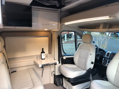 Inside an RV rental: Cream-colored interior with swivel seats, a flat-screen TV, & cozy dining. — photo 10