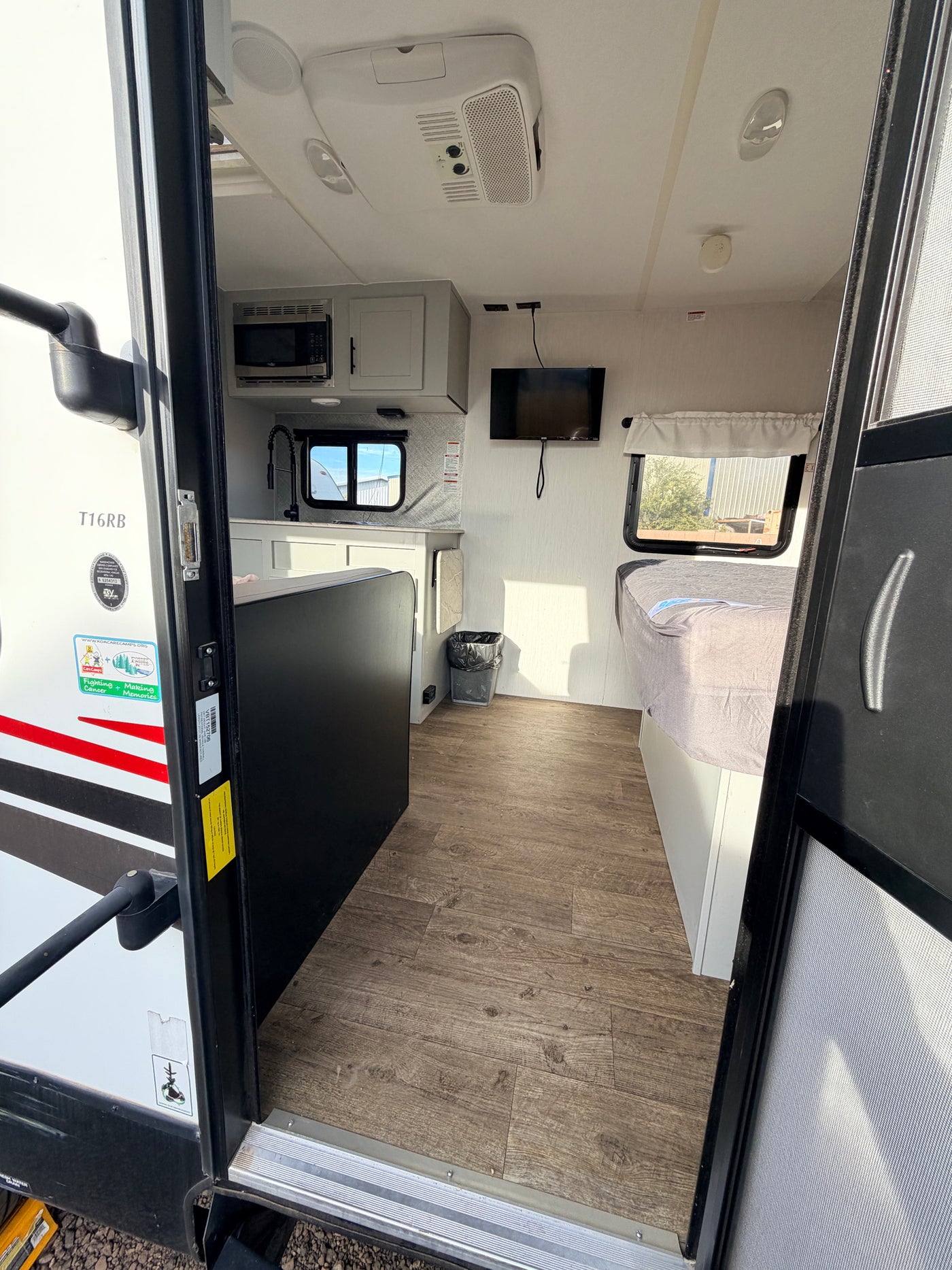 Bright rv rental interior from the doorway, showcasing a compact kitchen, bed, TV, and modern wood-look floor. — photo 14
