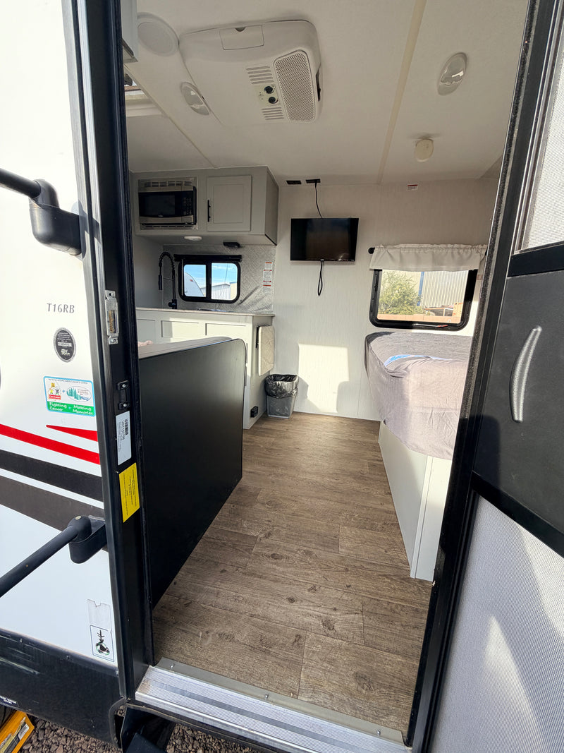 Bright rv rental interior from the doorway, showcasing a compact kitchen, bed, TV, and modern wood-look floor. — photo 14