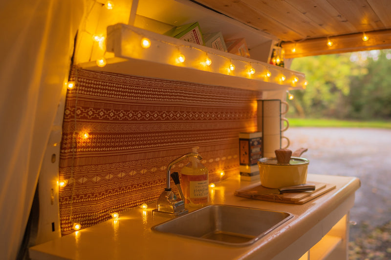 Cozy RV rental kitchen with warm string lights, a functional sink, and tea supplies on shelves, offering a welcoming vibe. — photo 9